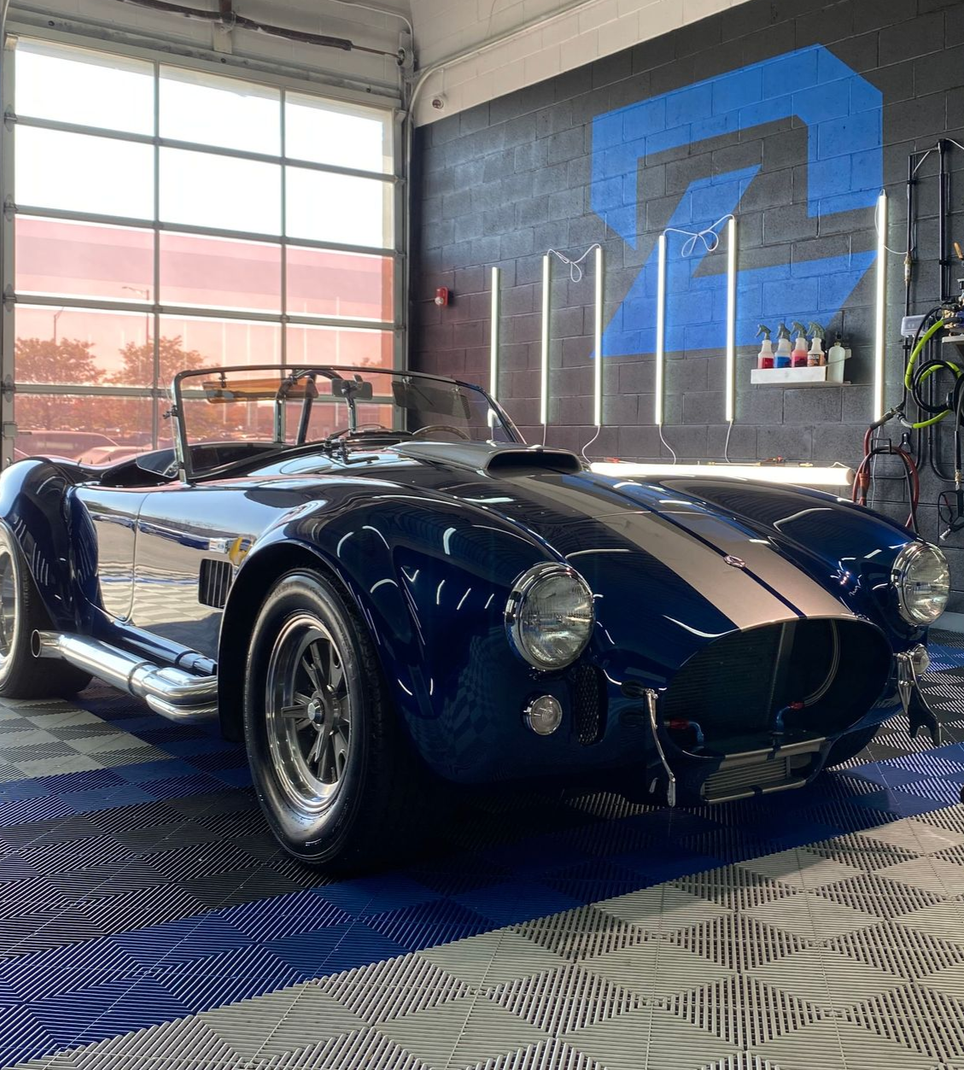Blue classic roadster sports car in a garage with checkered floor and blue wall mural
