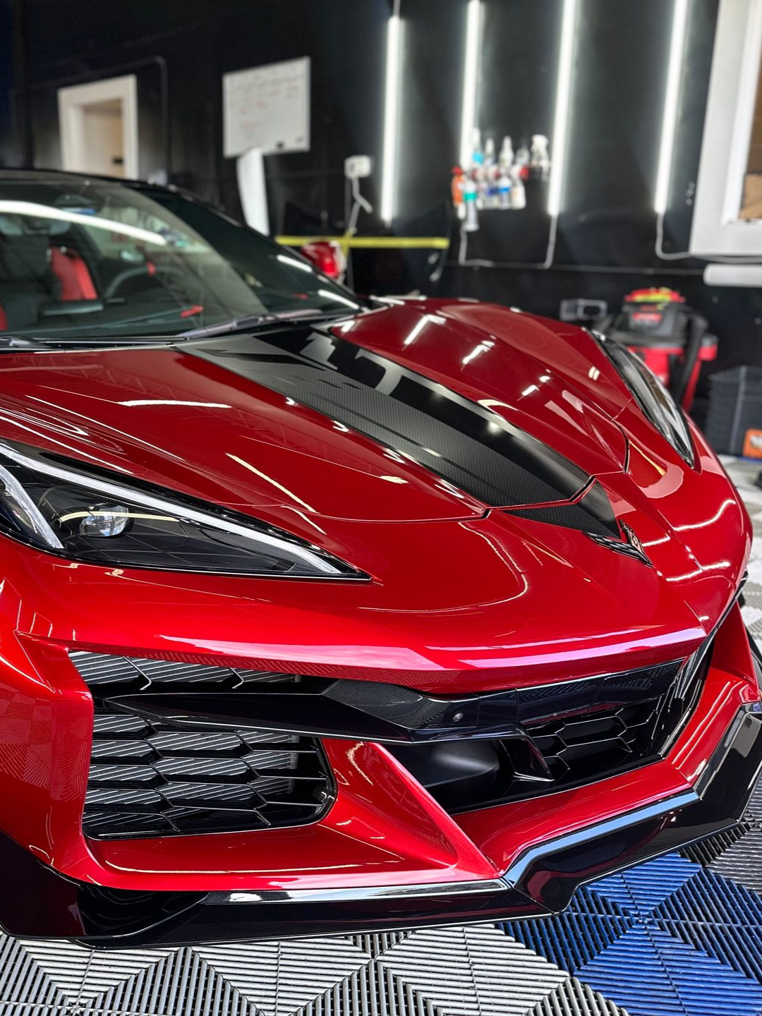 Red sports car with a glossy hood and black accents displayed indoors at an auto show.