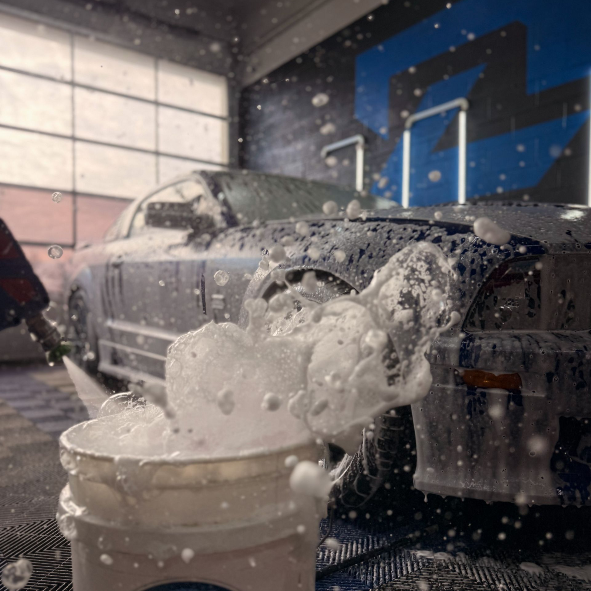 Foamy water splashing in a bucket beside a classic car in a car wash bay