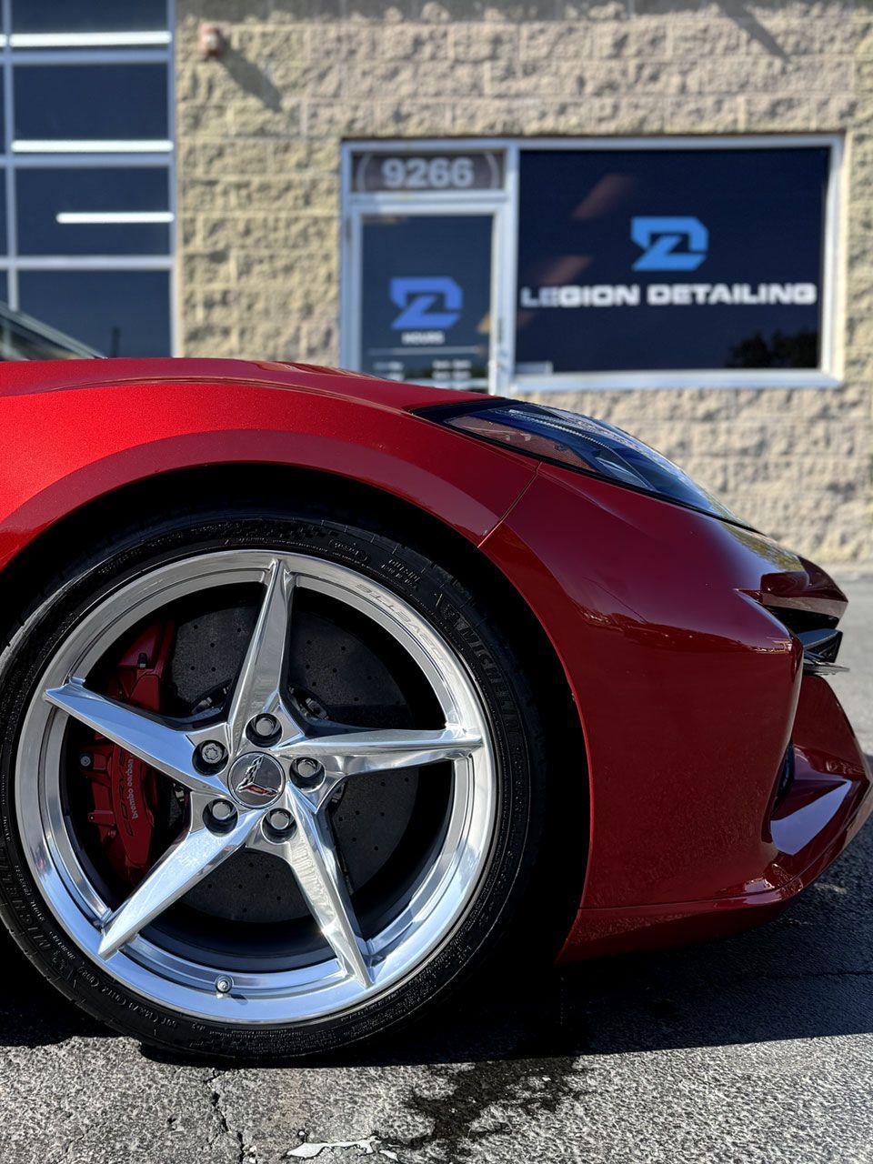 Close-up of a silver sports car’s front wheel with a chrome alloy rim and low-profile tire.