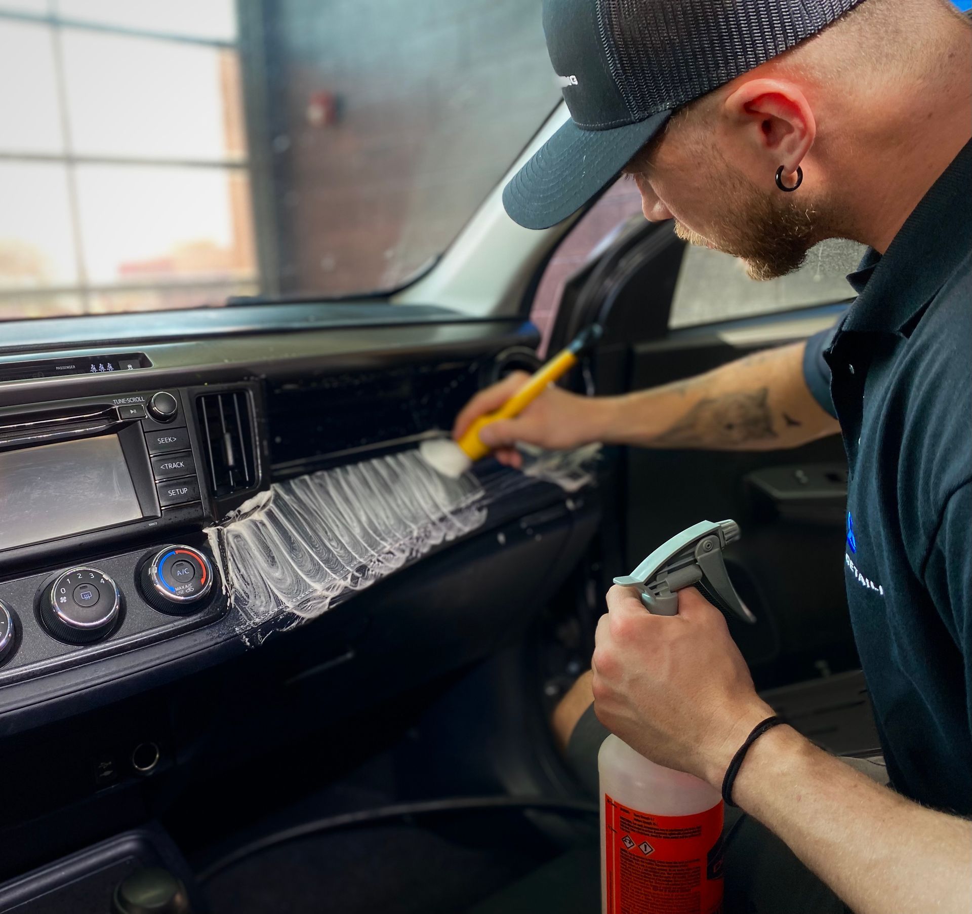 Detailing a car dashboard with spray and brush inside a vehicle