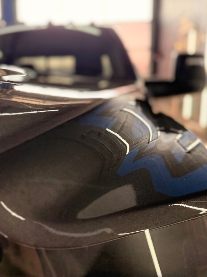 Close-up of a glossy black race car body panel with blue accents in a workshop