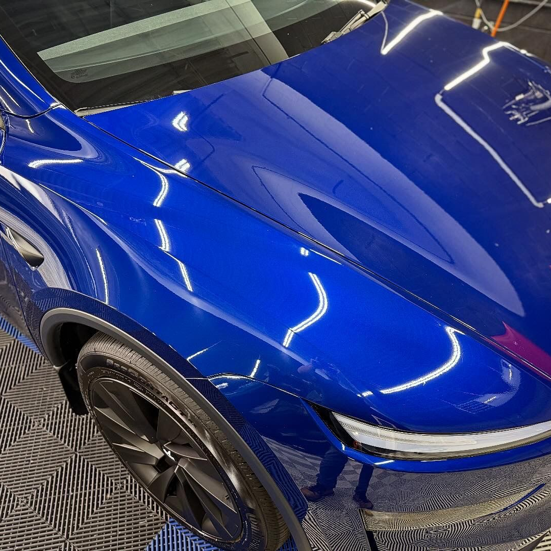 Blue sports car hood and front fender with glossy reflections, close-up view