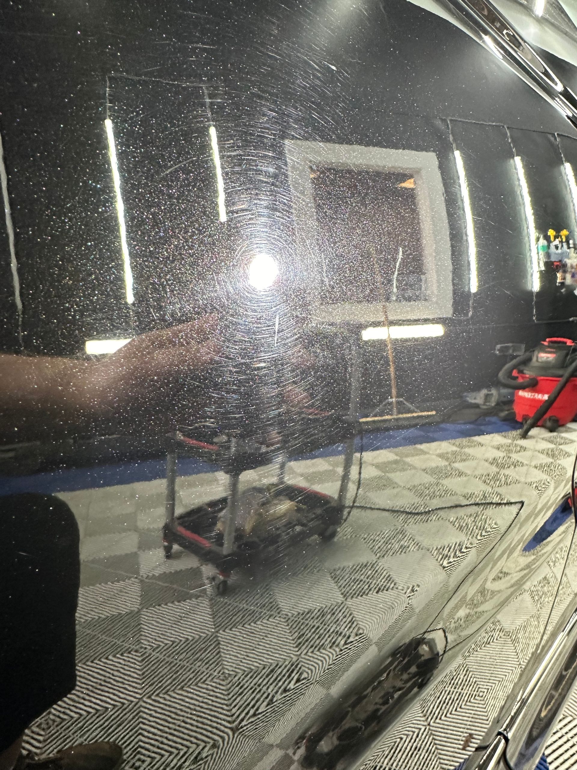Rain-speckled car window reflecting a lit patio with a table, chair, and red object at right