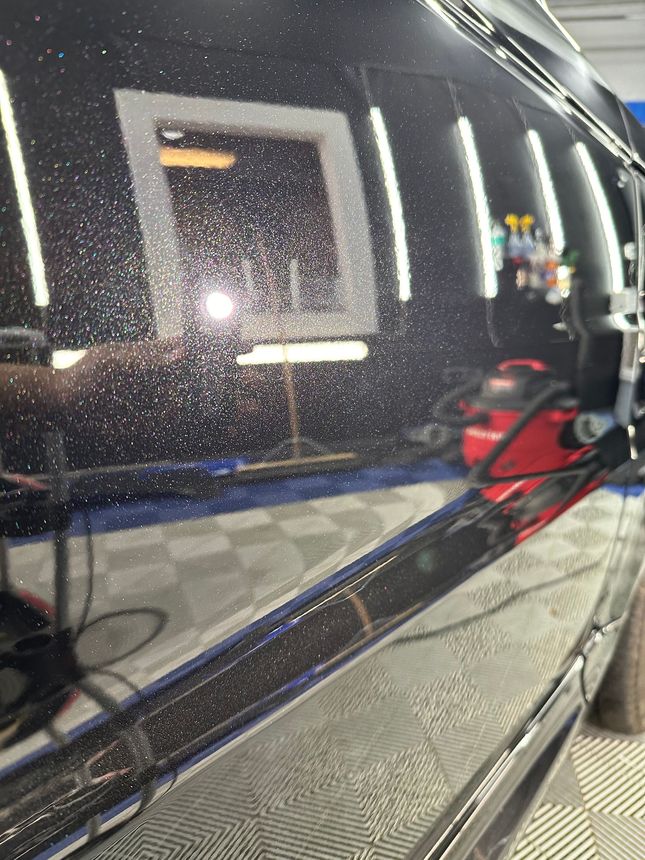 Black car side mirror and glossy door reflecting a garage, with a red bag on the seat inside.