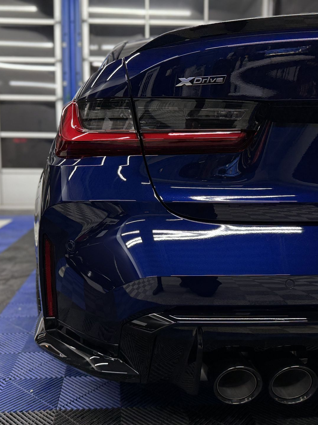 Rear view of a blue sports sedan with black trim and quad exhaust pipes in a garage.