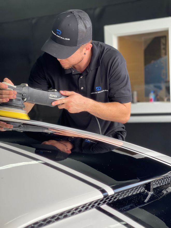 Mechanic polishing a black car roof with a buffer in a garage