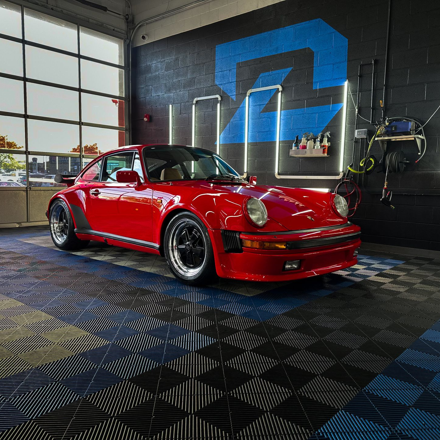 Red classic Porsche 911 in a garage with a blue wall mural and checkered floor.