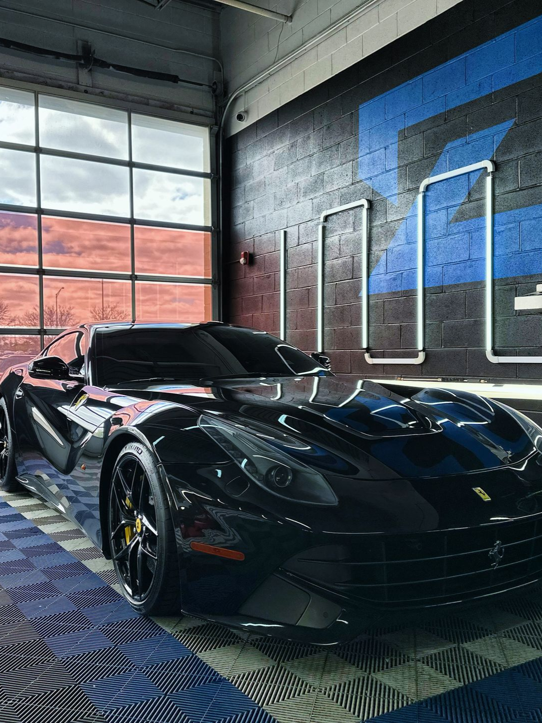 Black sports car in a garage with large windows and blue wall accents