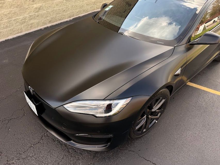 Matte black Tesla sedan parked in a lot, viewed from the front-left side.