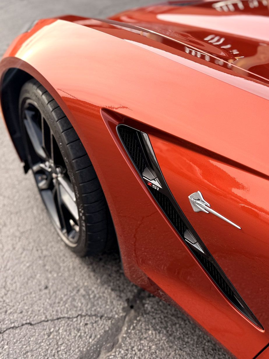 Red sports car parked on a tree-lined street under bright green leaves