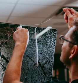 Person with glasses stretching a transparent wire over a black panel indoors