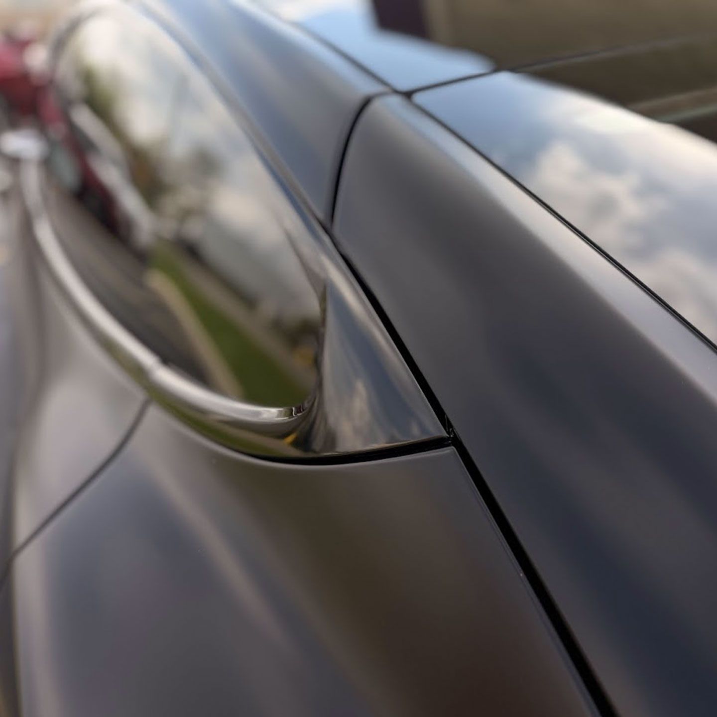 Close-up of a black car’s side mirror and glossy door panel reflecting the sky.