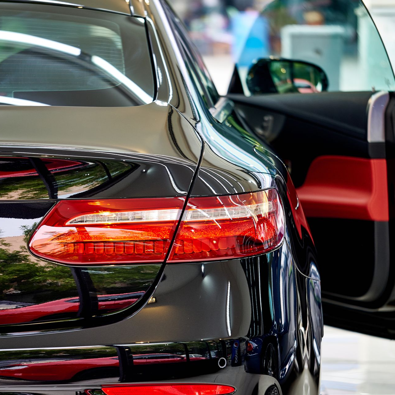 Black car rear with red taillight and open door inside a showroom
