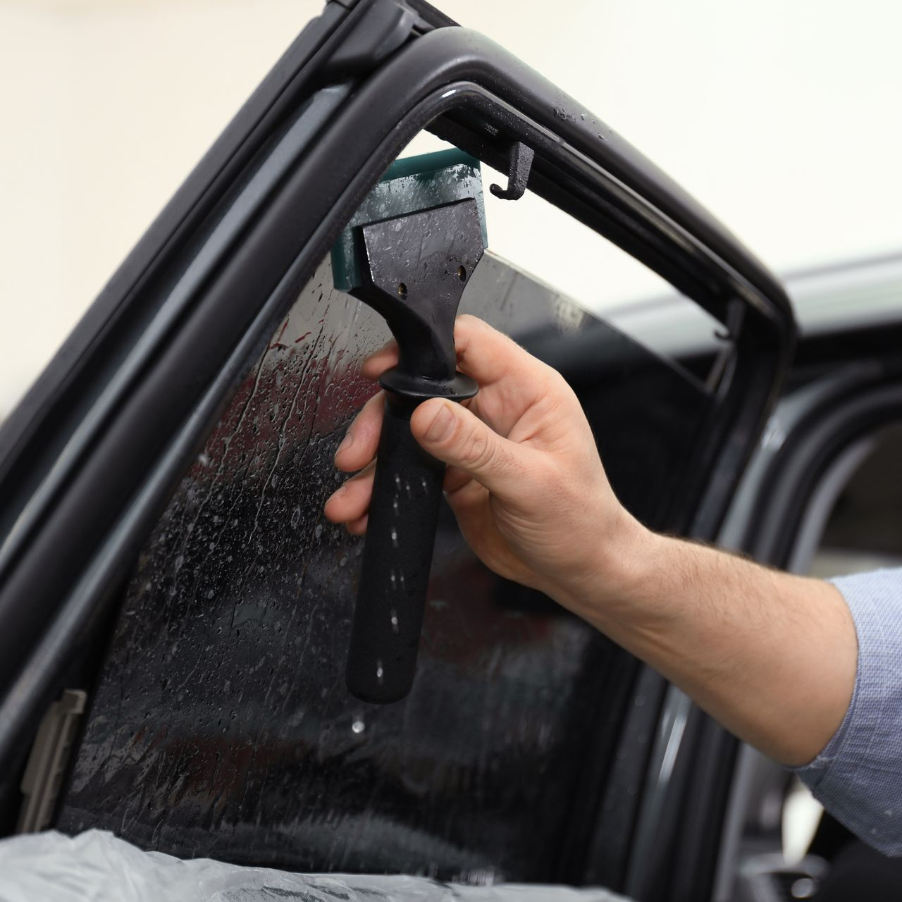 Hand using a squeegee to clean a car window on an open car door