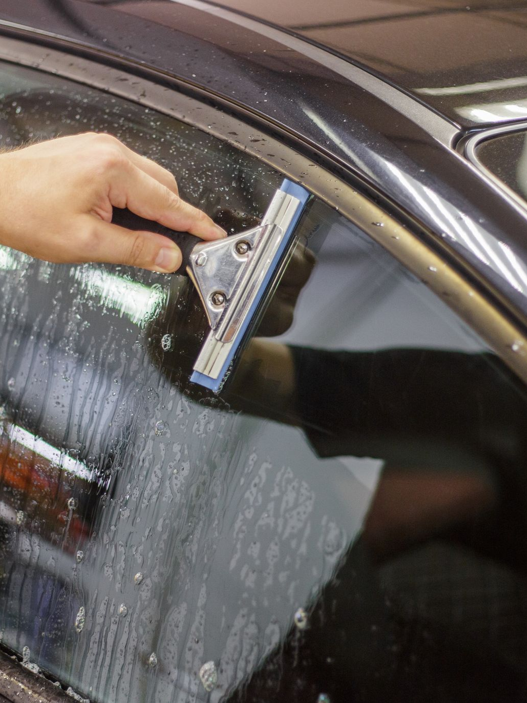 Hand using a window squeegee on a wet car windshield