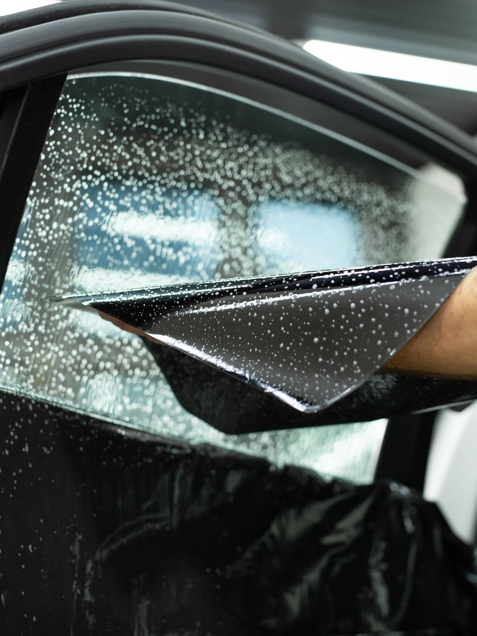 Hand peeling black film from a car window with shattered safety glass visible underneath