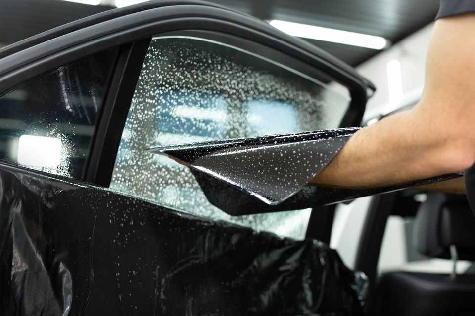 Hand applying black window tint film to a car side window inside a garage