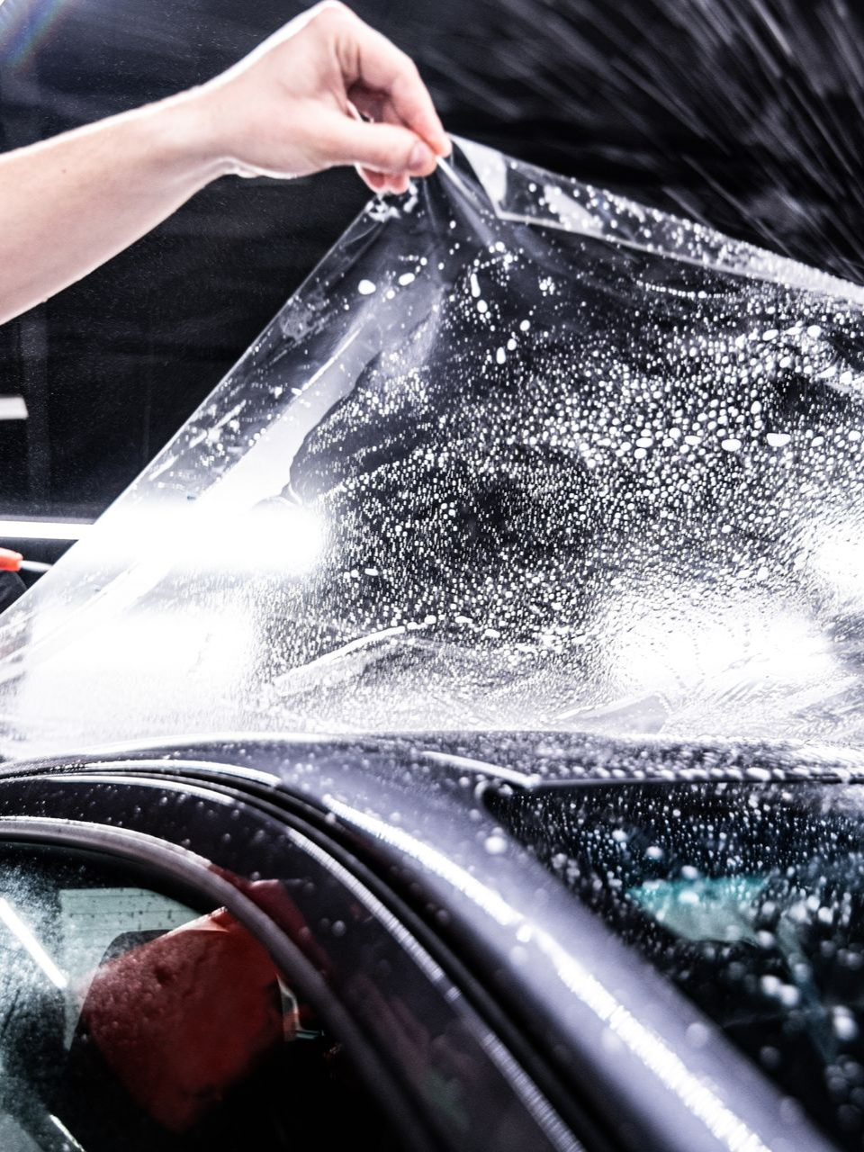 Hand peeling clear film from a wet car windshield during window tinting or cleaning