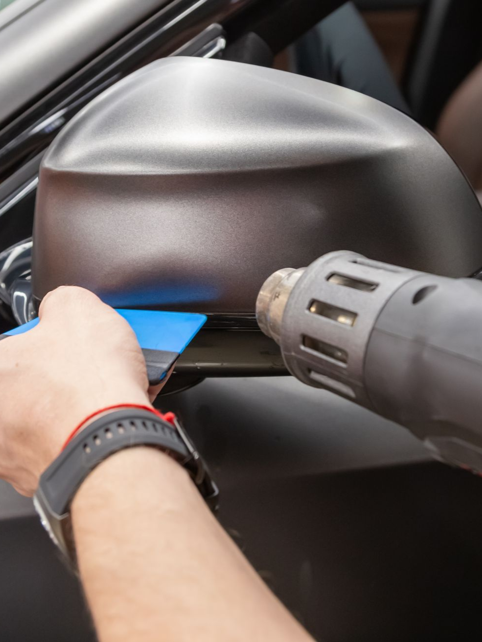 A person is applying a clear film to the hood of a car.