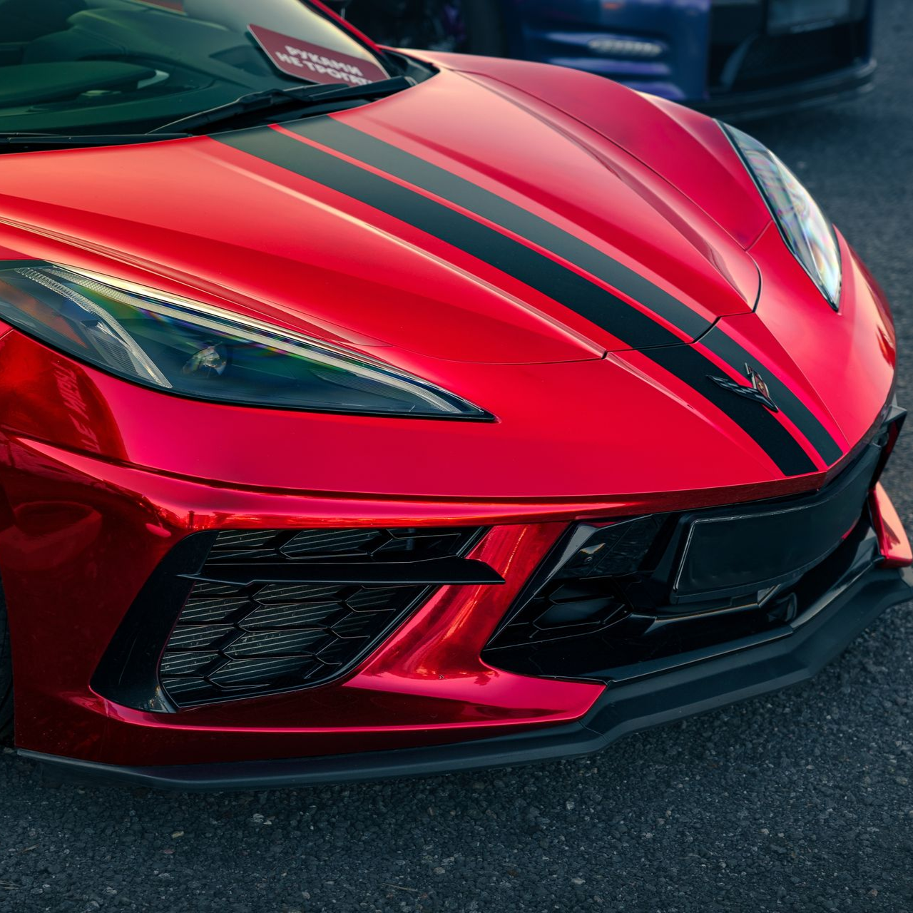 A person wearing black gloves is polishing the hood of a red car.