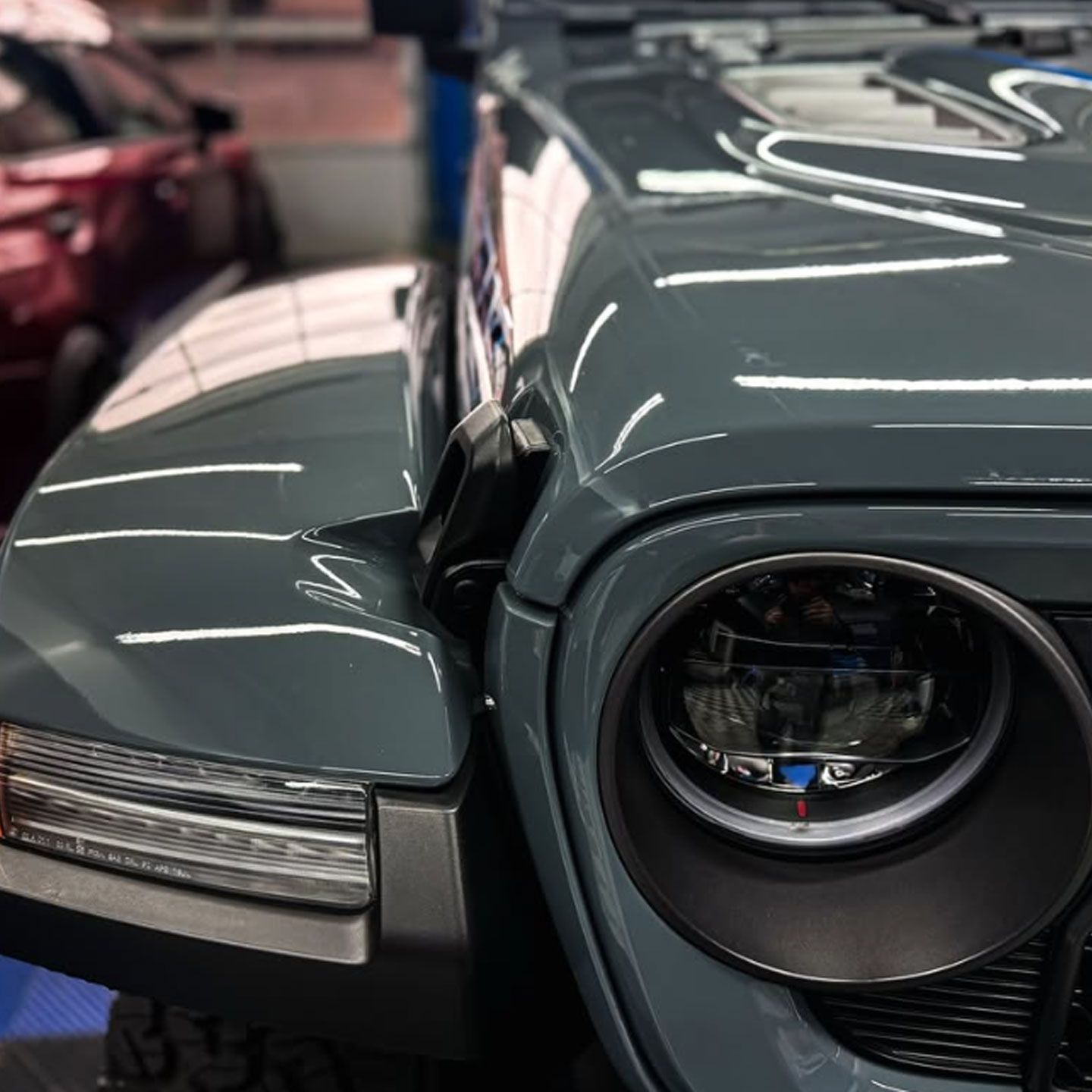 Close-up of a gray classic car’s front end with round headlight and chrome trim.