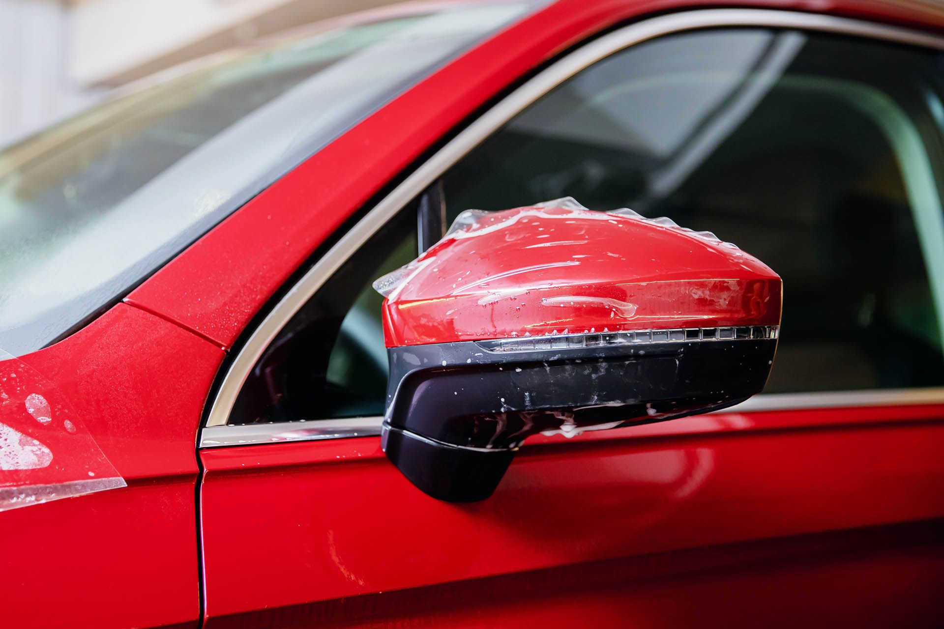 Close-up of a red car’s side mirror with black housing and glossy paint.