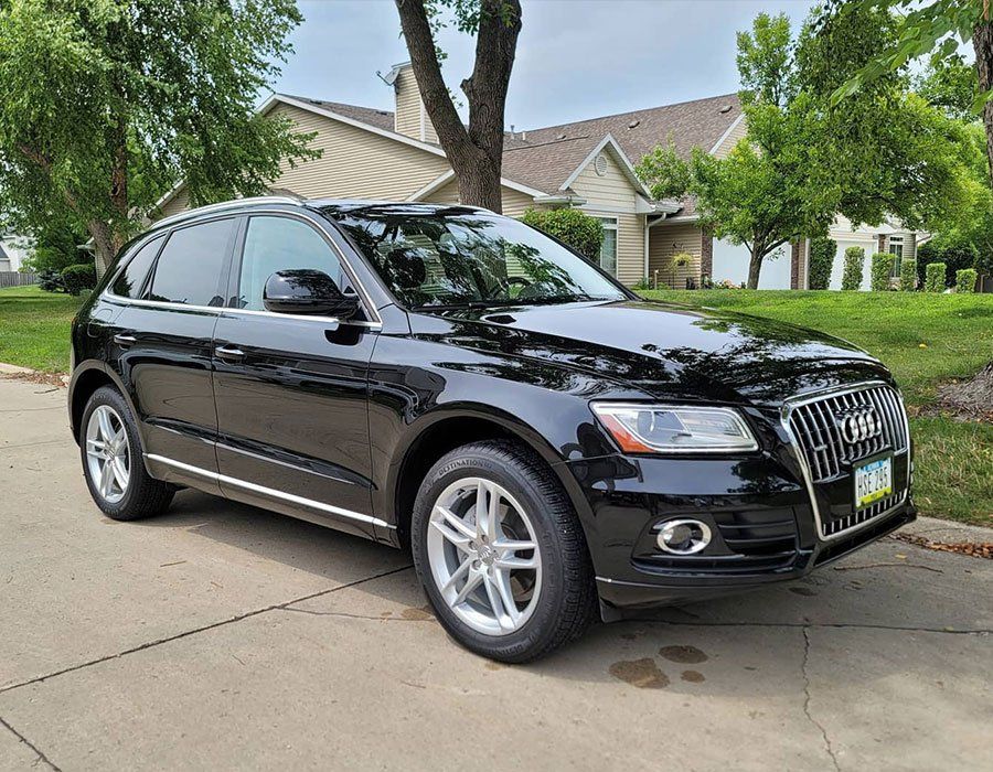 A black audi q5 is parked in a driveway in front of a house.