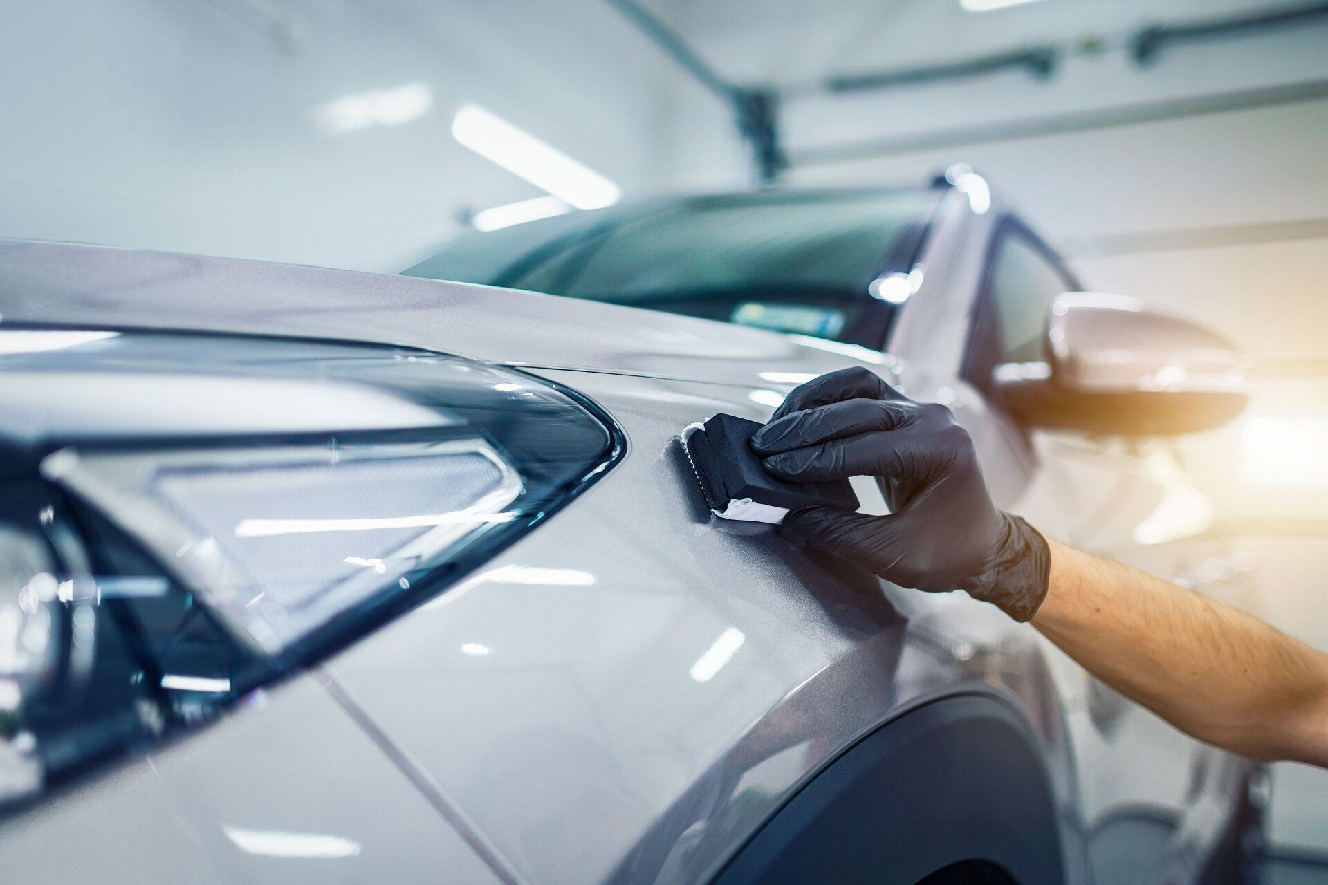 Gloved hand polishing a white car’s side panel in a bright auto shop