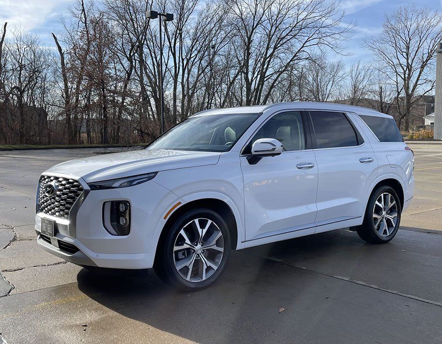 White SUV parked on a wet lot with bare trees in the background