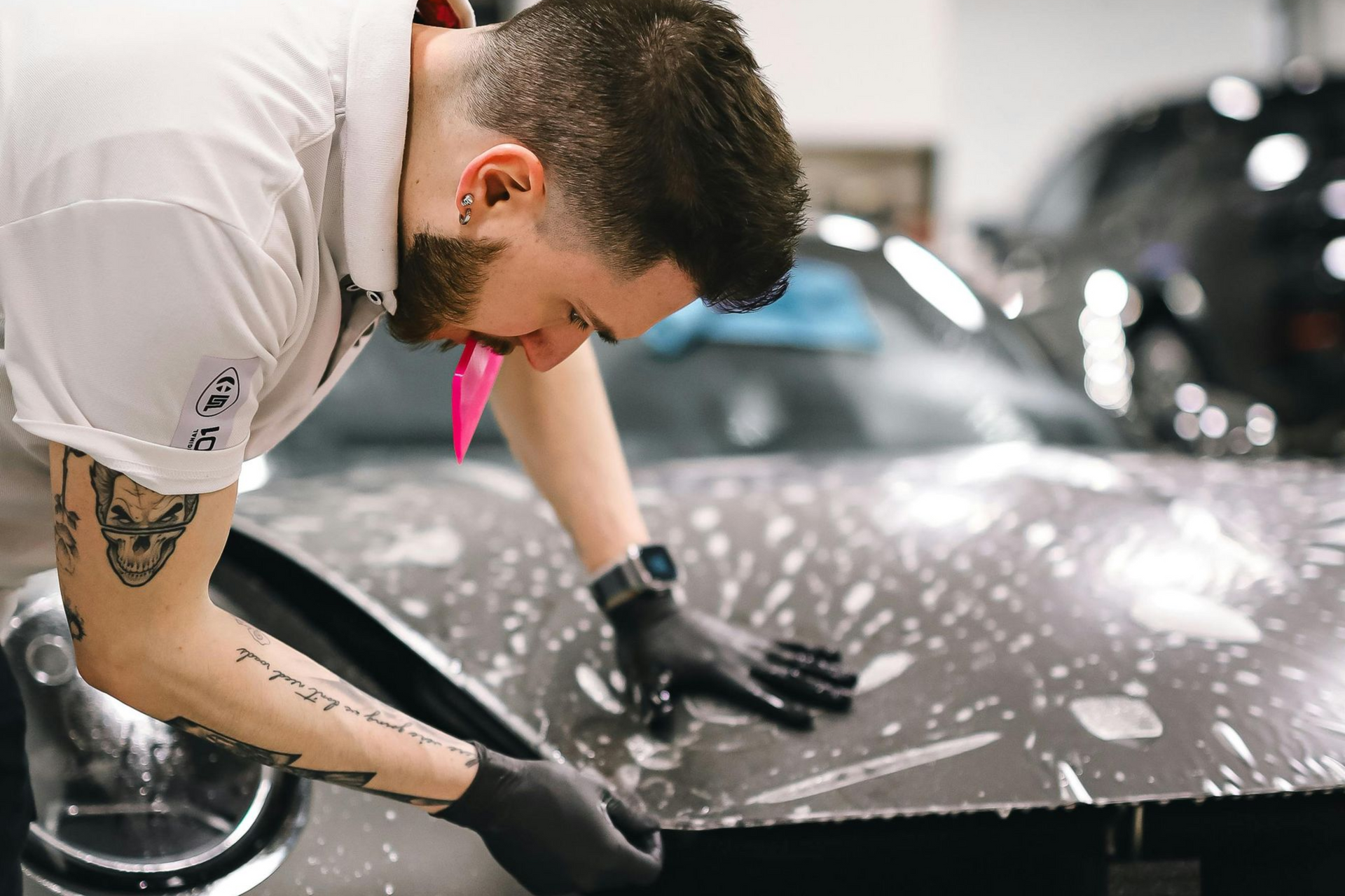 Detailer polishing a black car hood with a cloth in a garage