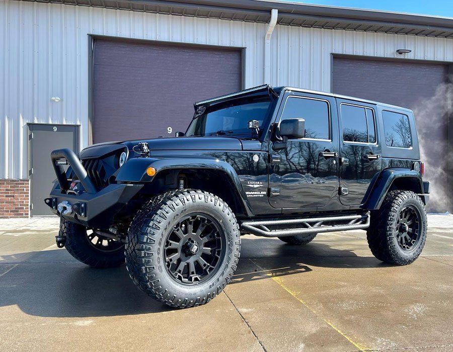 A black jeep is parked in front of a building.