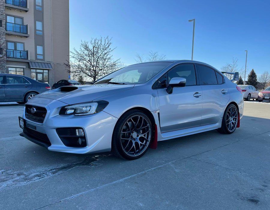 A silver subaru wrx sti is parked in a parking lot in front of a building.