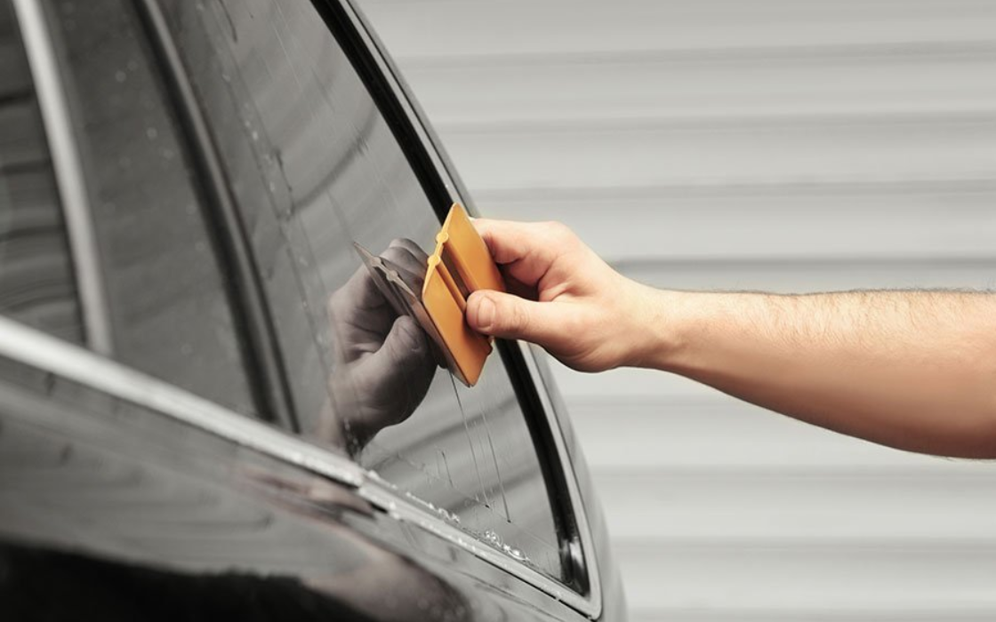 Hand wiping a black car window with an orange cloth near a side mirror