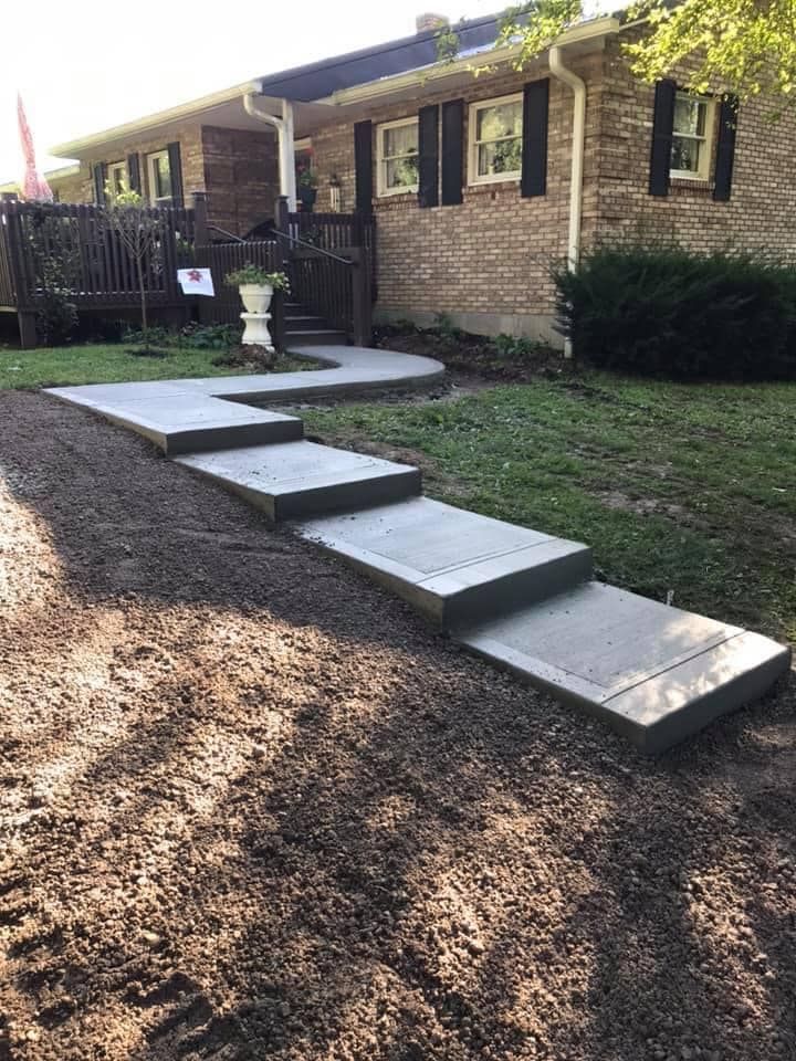 Front entrance with wide concrete steps leading up a brick house, with a small fountain beside the walkway.