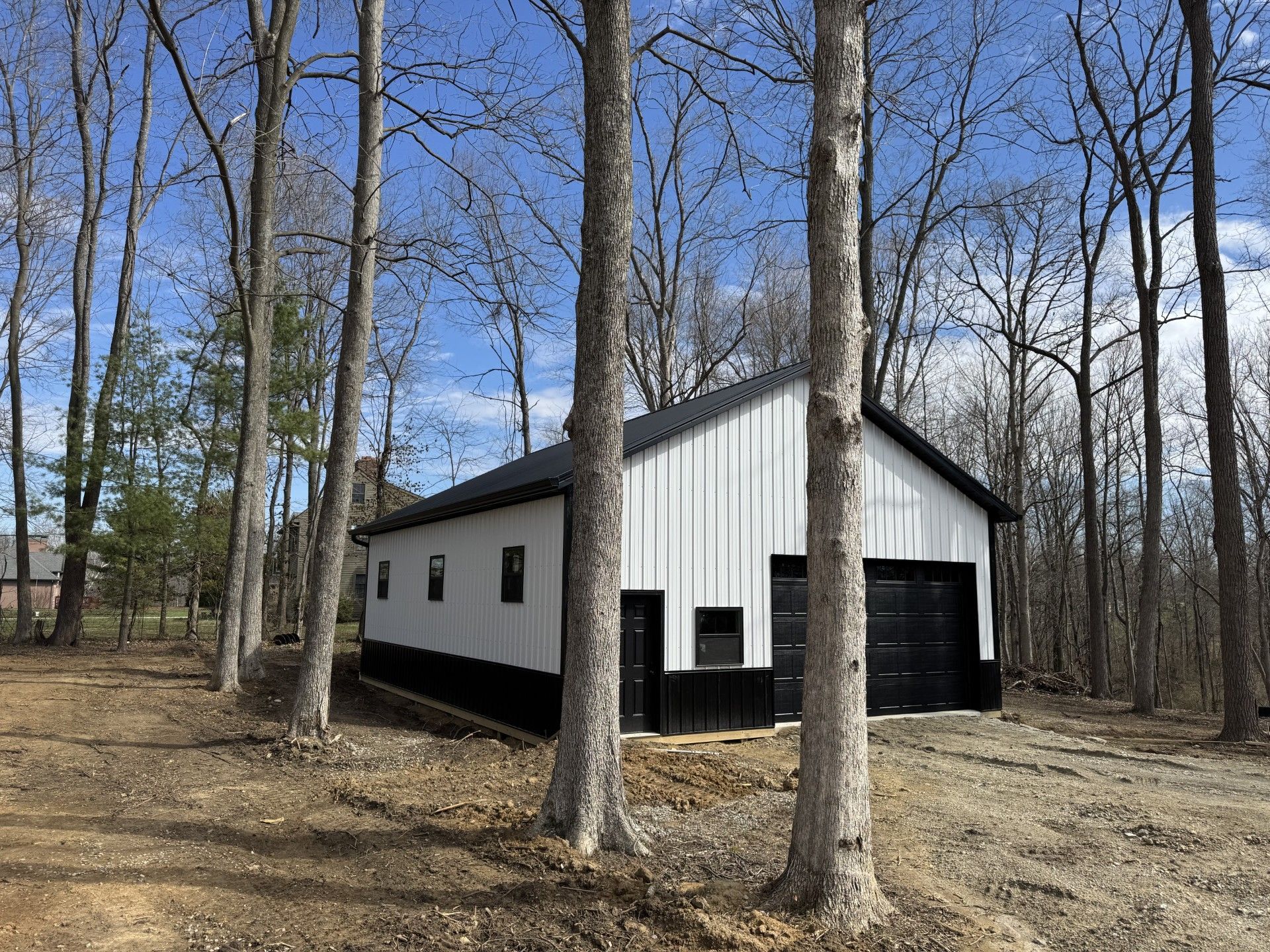 White cabin with black trim in a leafless wooded area under a blue sky