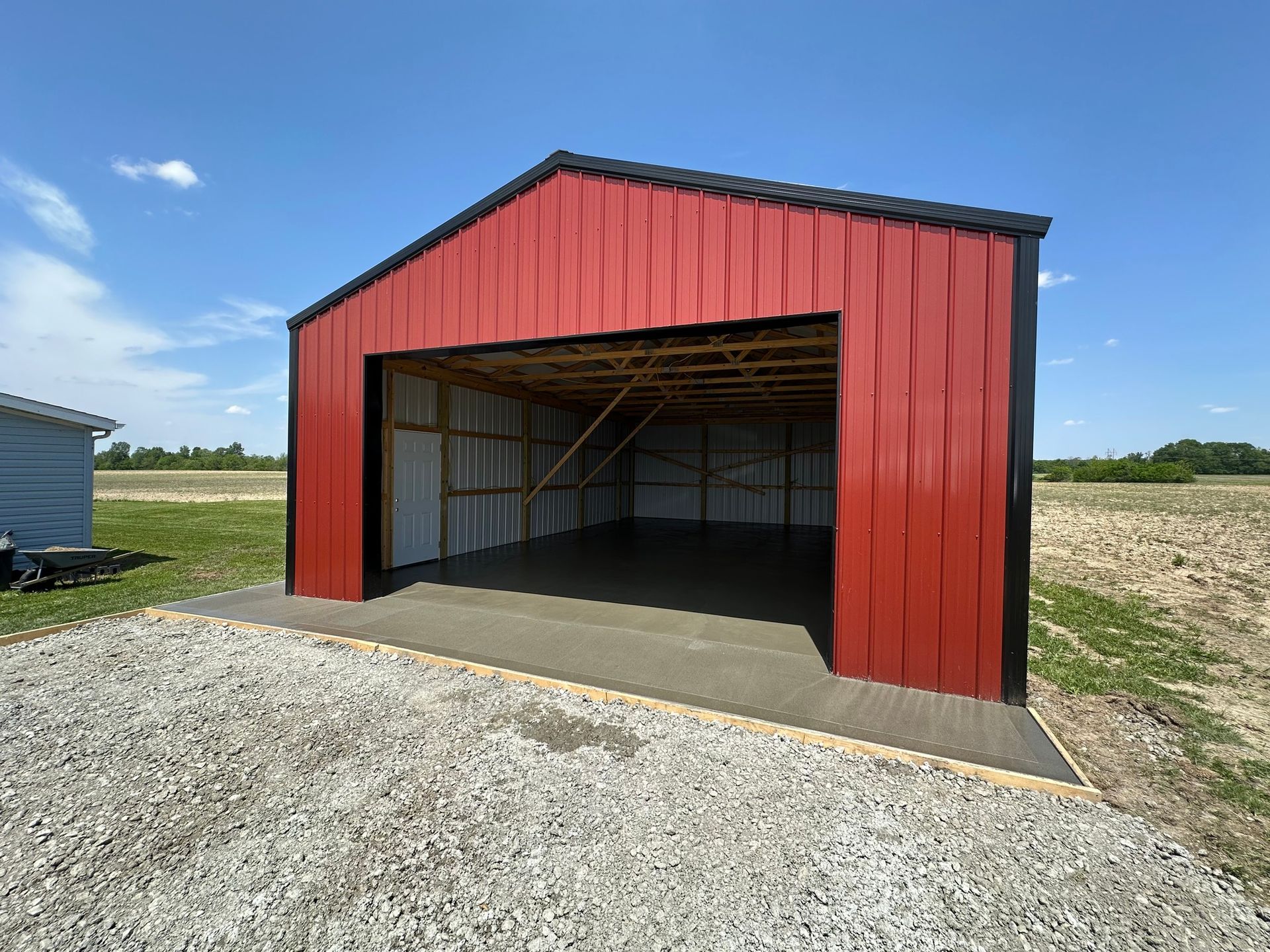 Red metal garage with open front on a gravel lot under a blue sky