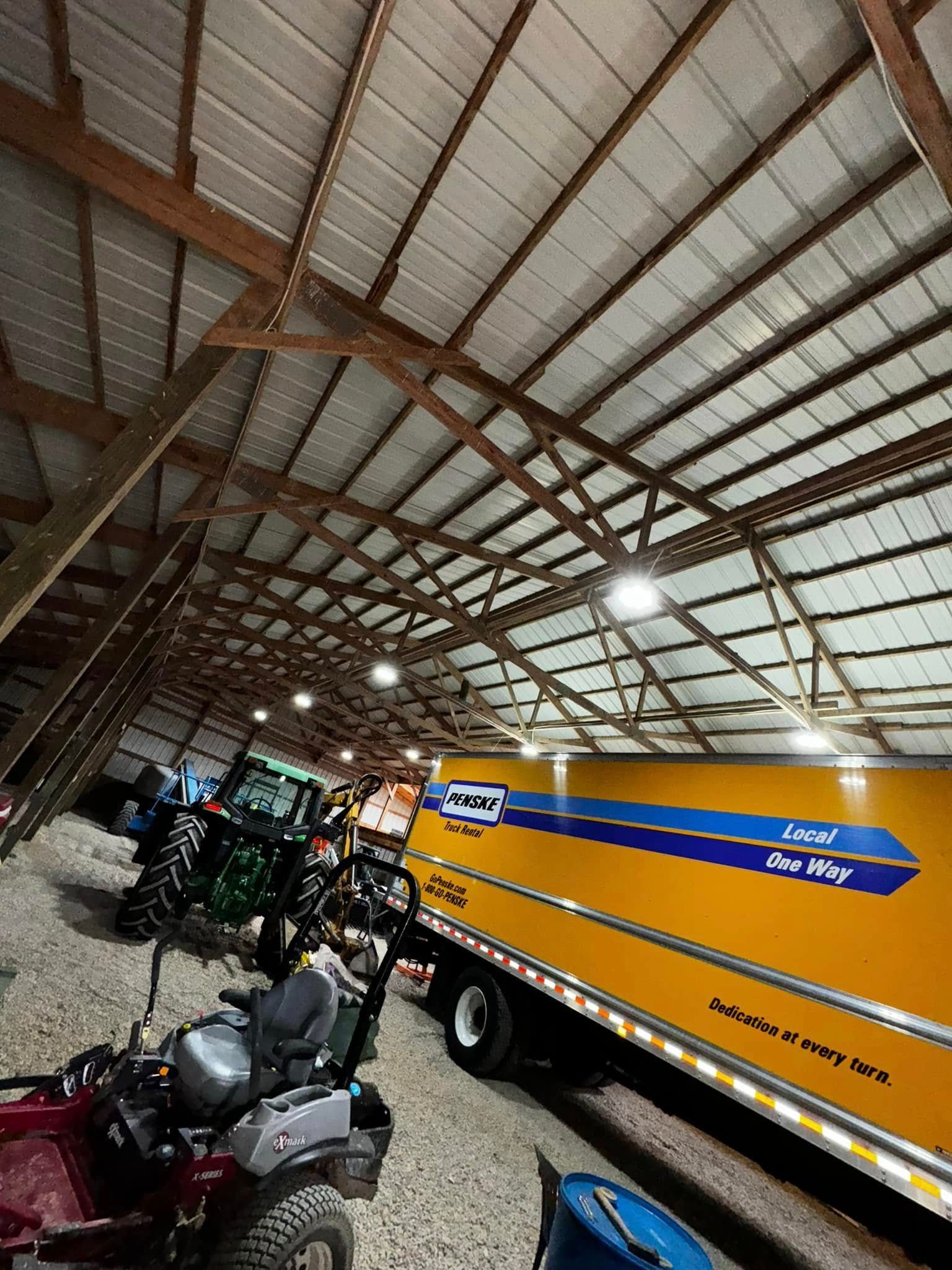 Covered shed with a yellow tanker truck, parked ATVs, and farm equipment under a metal roof.