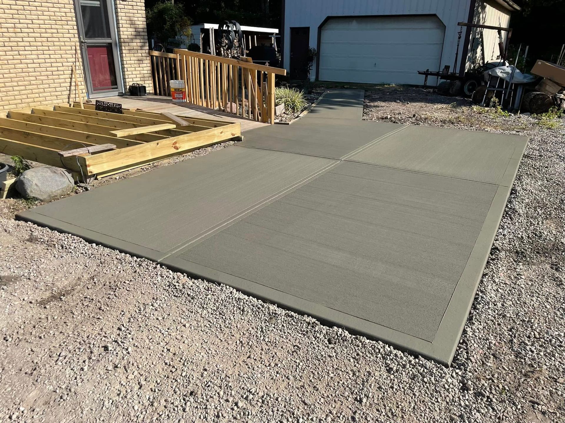 Large concrete patio slab in a gravel driveway beside a house and garage