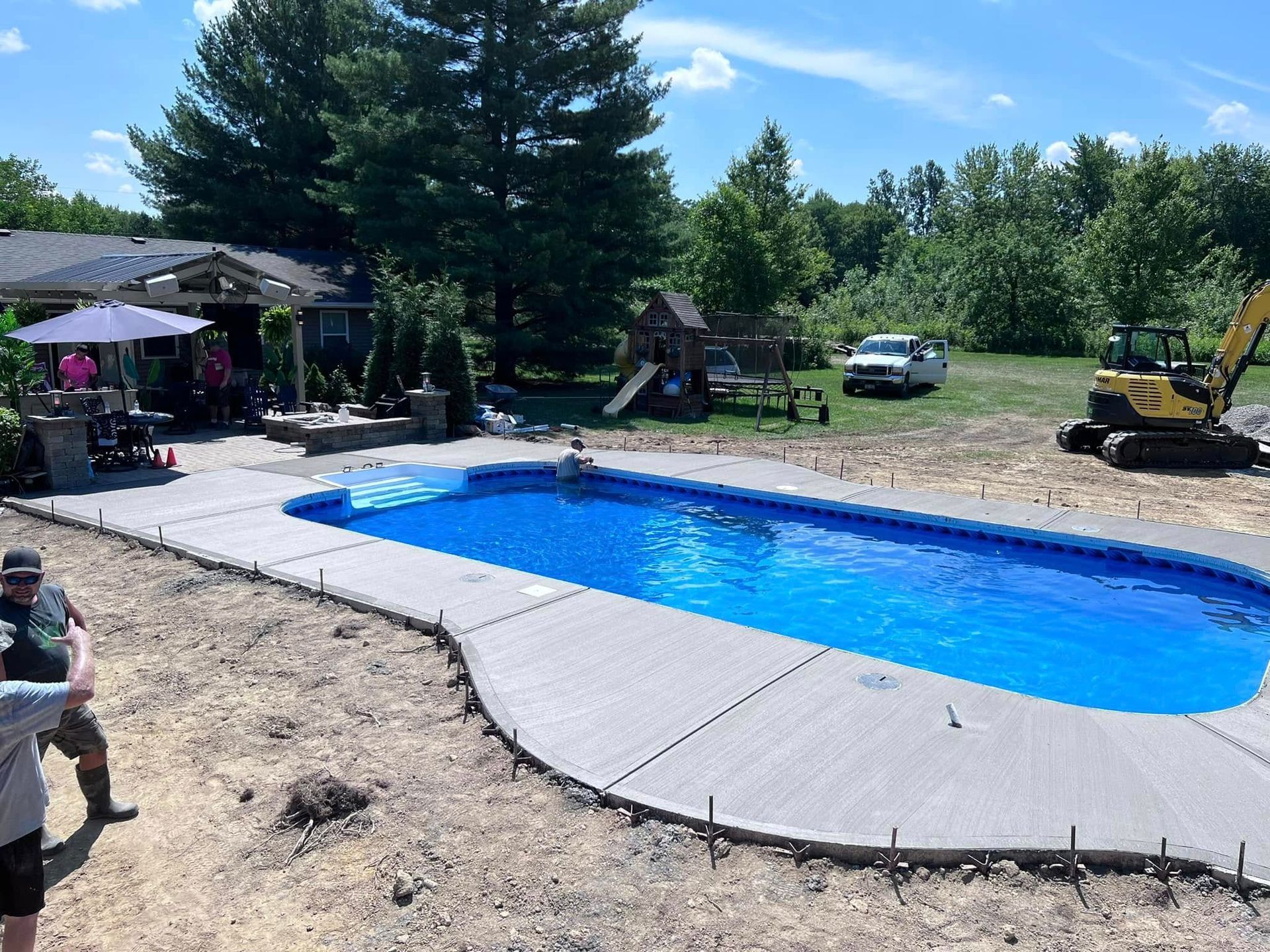 Backyard pool under construction with blue liner, concrete deck, trees, and work equipment nearby