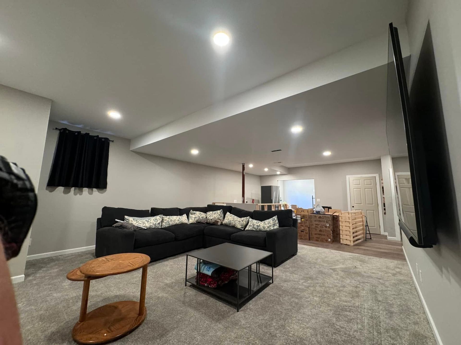 Modern basement living room with gray sectional, round wooden table, and recessed ceiling lights.