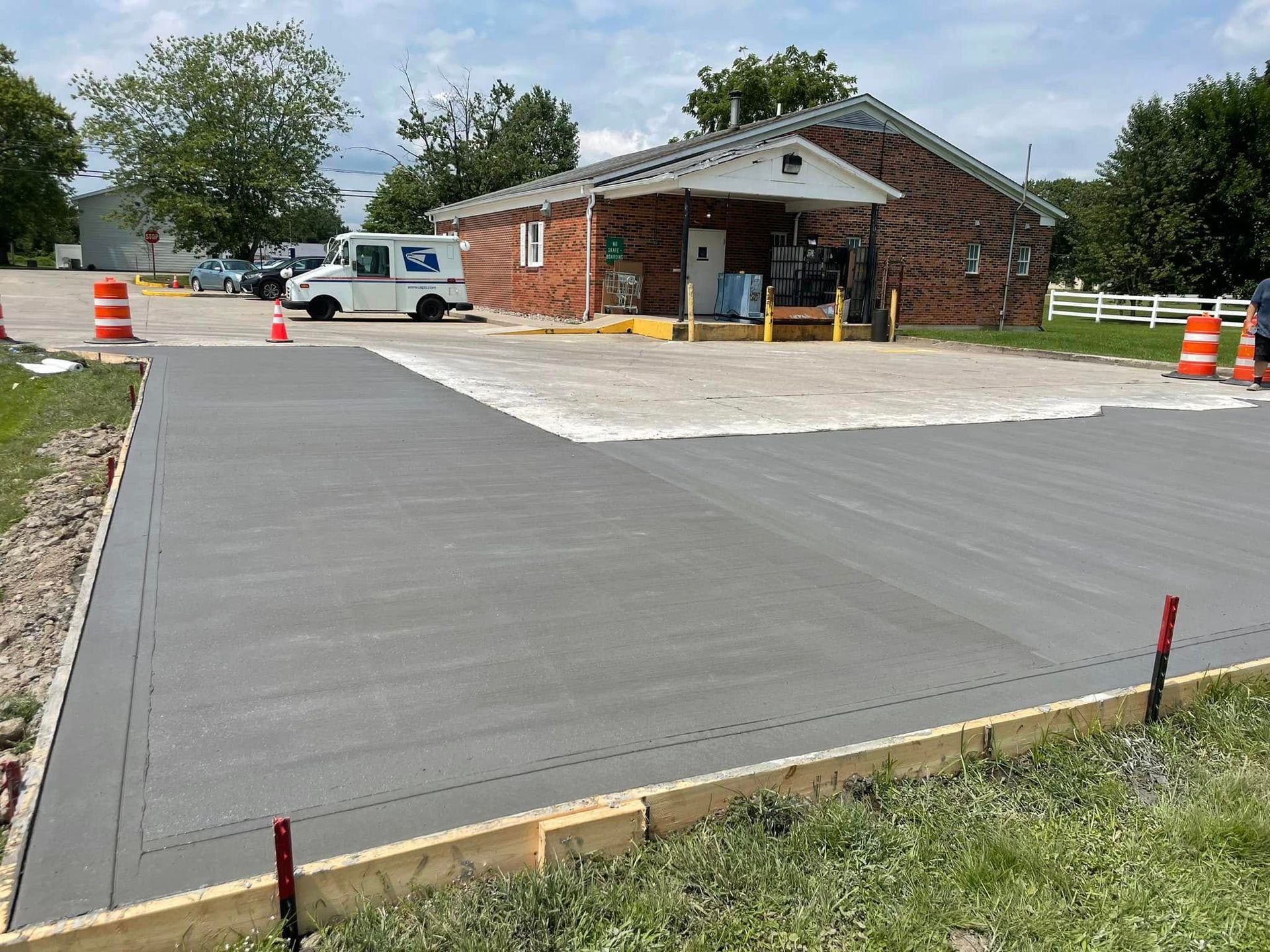 Freshly paved parking lot beside a small brick building with orange cones and a white van.