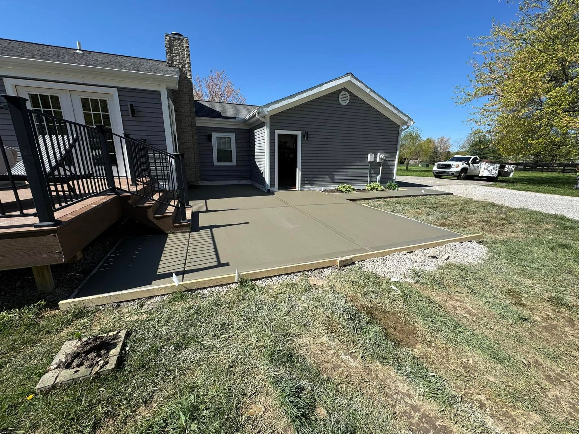 Backyard concrete patio beside a gray house and garage, with a small deck and grassy yard