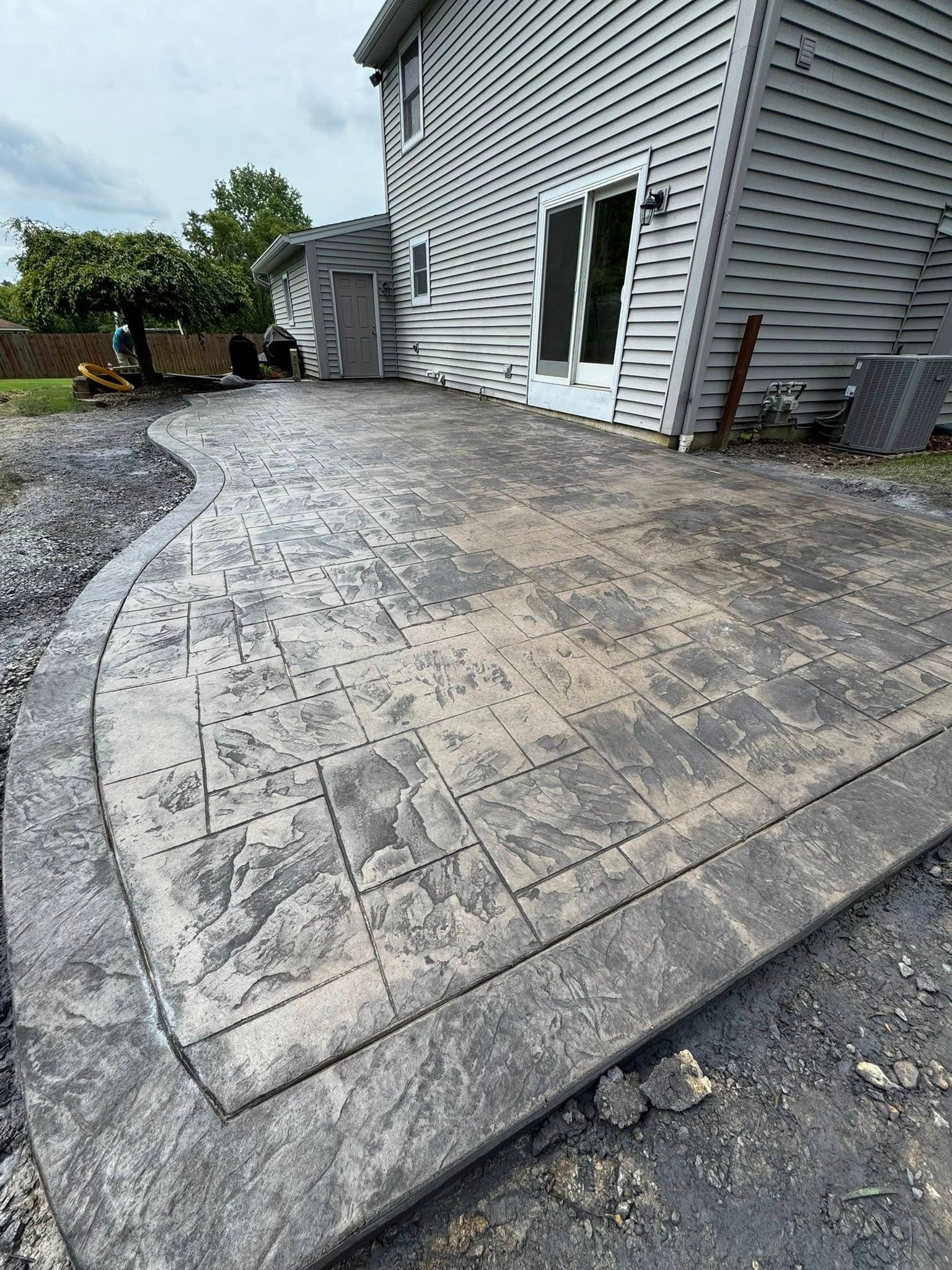 Curved concrete patio beside a house with white siding, adjacent to gravel and a backyard area