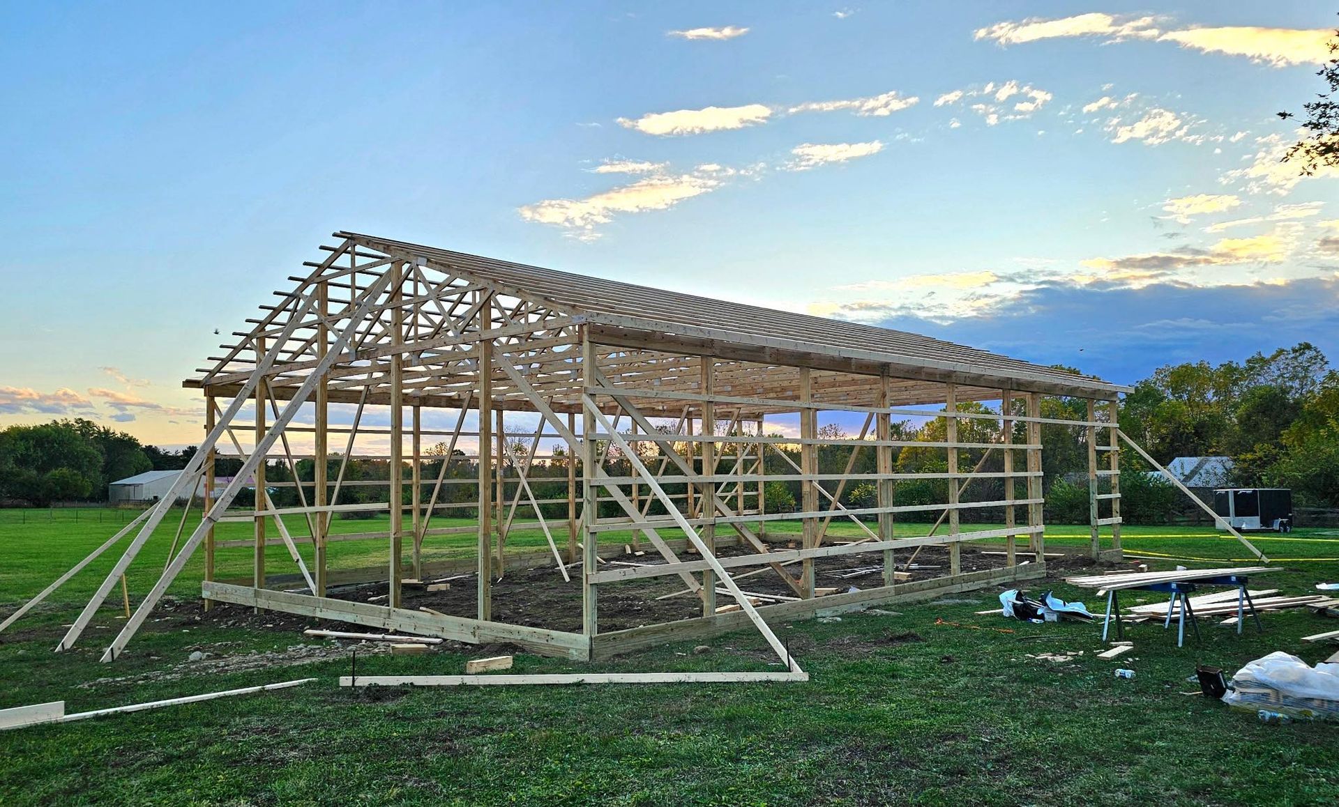 Wooden barn frame under construction in a grassy field at sunset