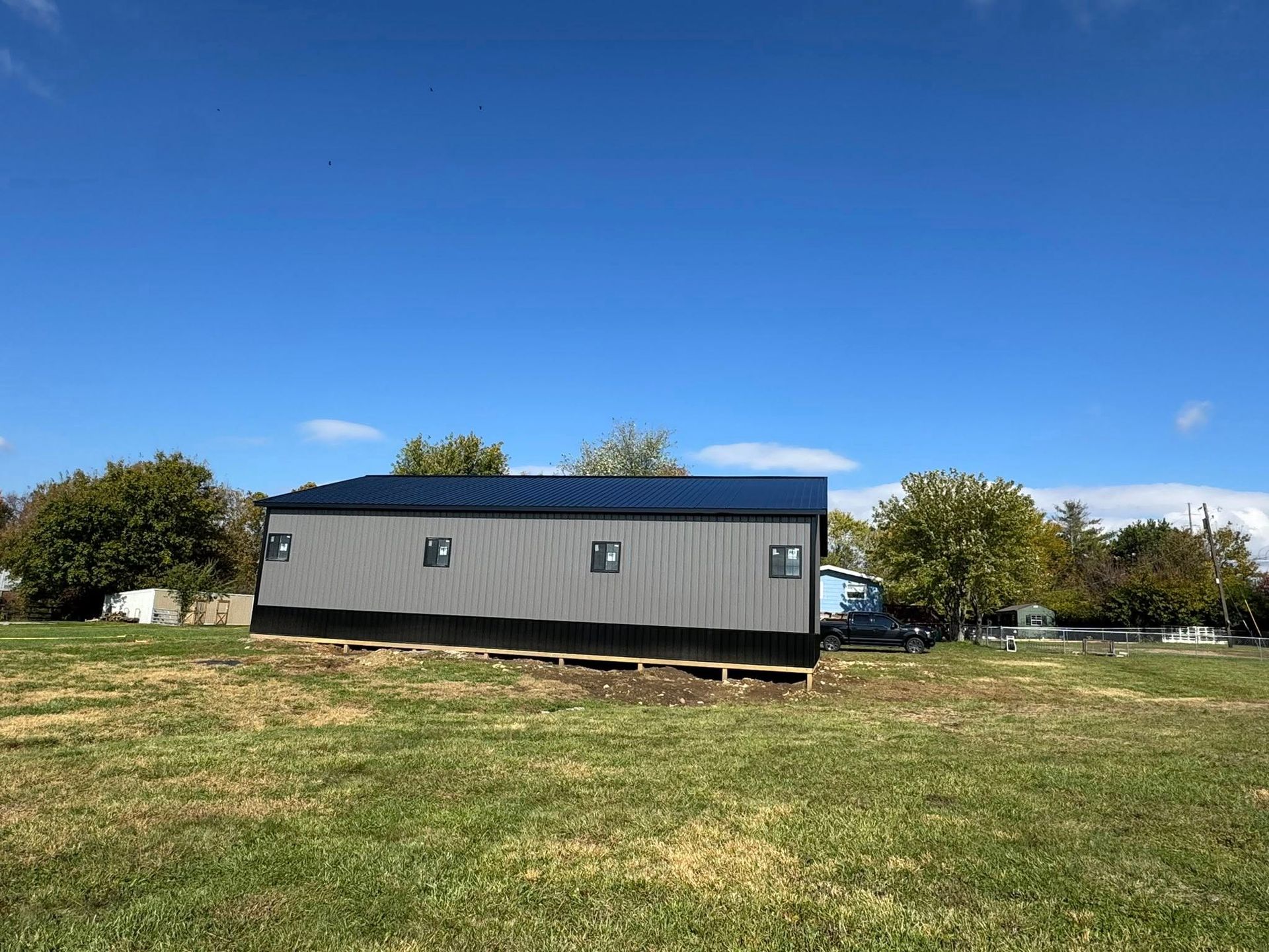 Gray mobile home in a grassy field under a clear blue sky.