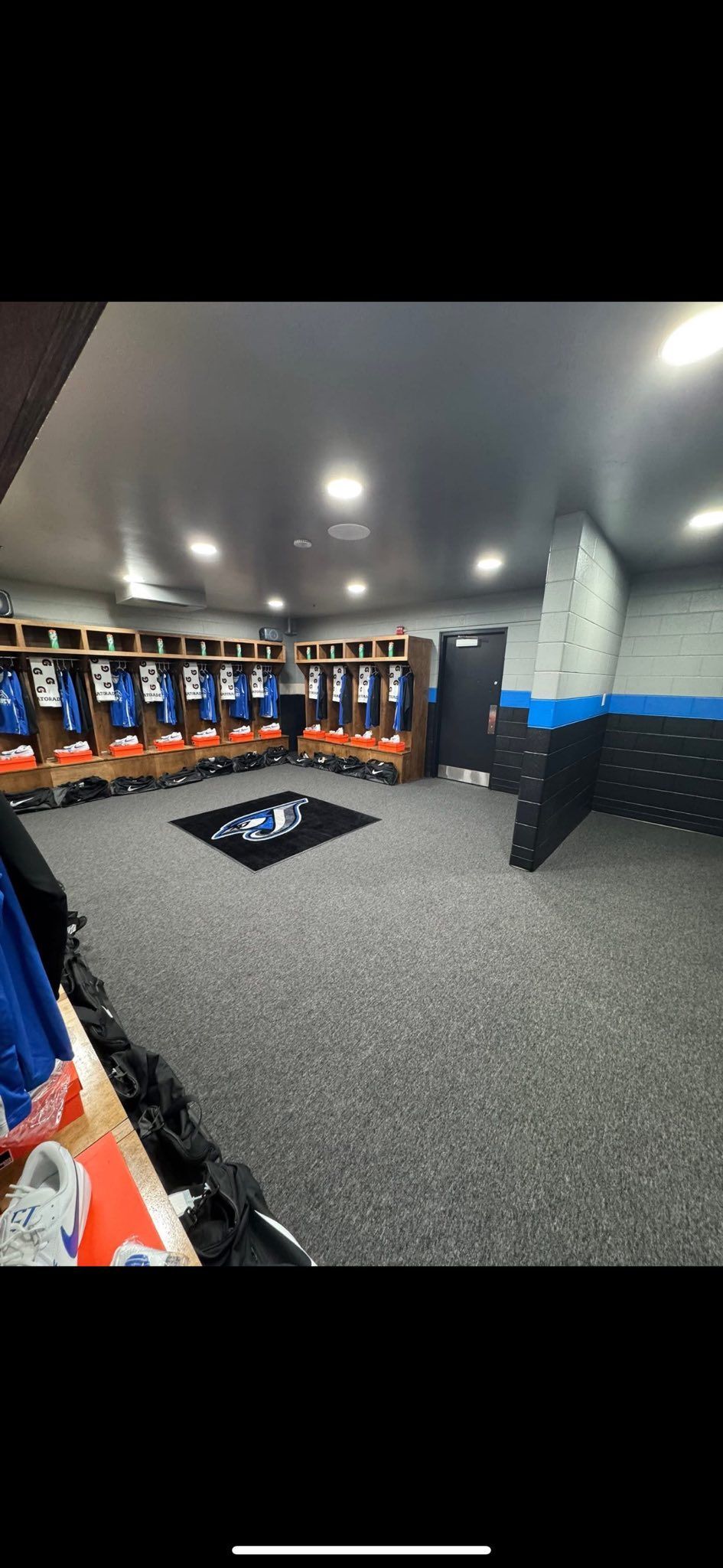 Sports locker room with blue and orange lockers, gray carpet, and a black bench in the center