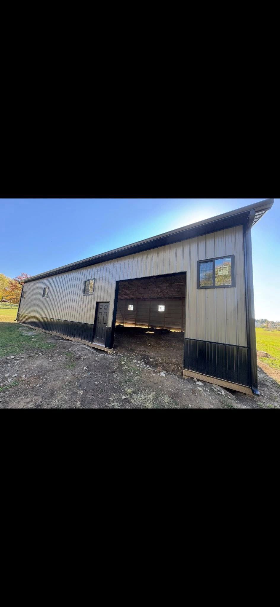White metal barn with open garage door on a gravel lot under a clear blue sky