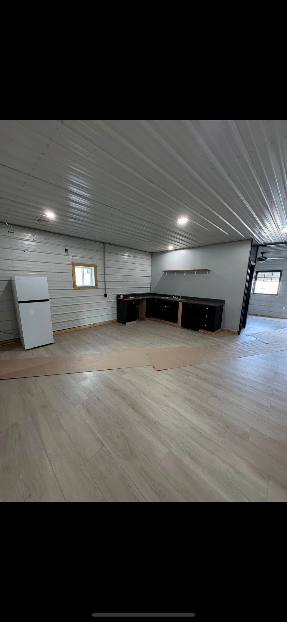 Empty modern room with wood floor, white walls, black cabinets, and bright ceiling lights