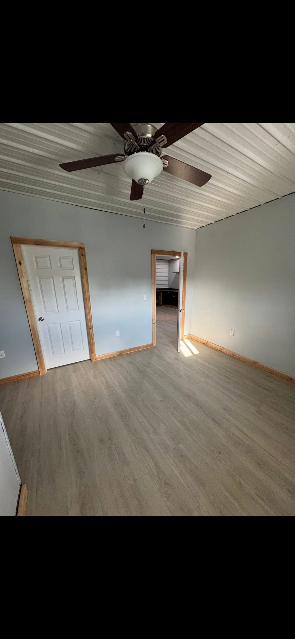 Empty bedroom with wood floor, white paneled walls, ceiling fan, and two doorways